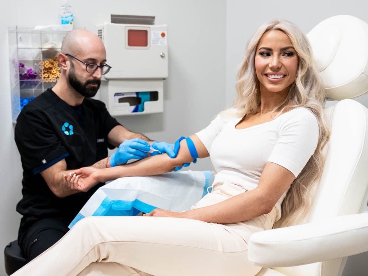 A smiling patient relaxes in a chair while a clinician draws her blood