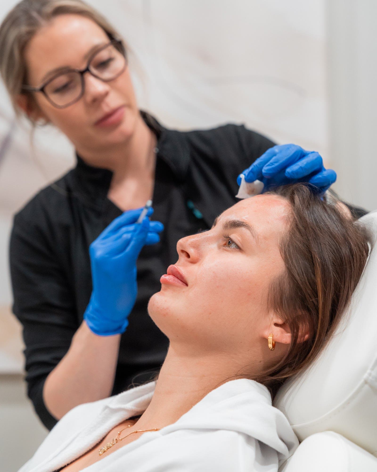 An injector prepares a careful filler treatment for a patient in profile
