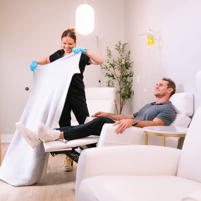 A clinician drapes a warm blanket over a patient during an IV infusion