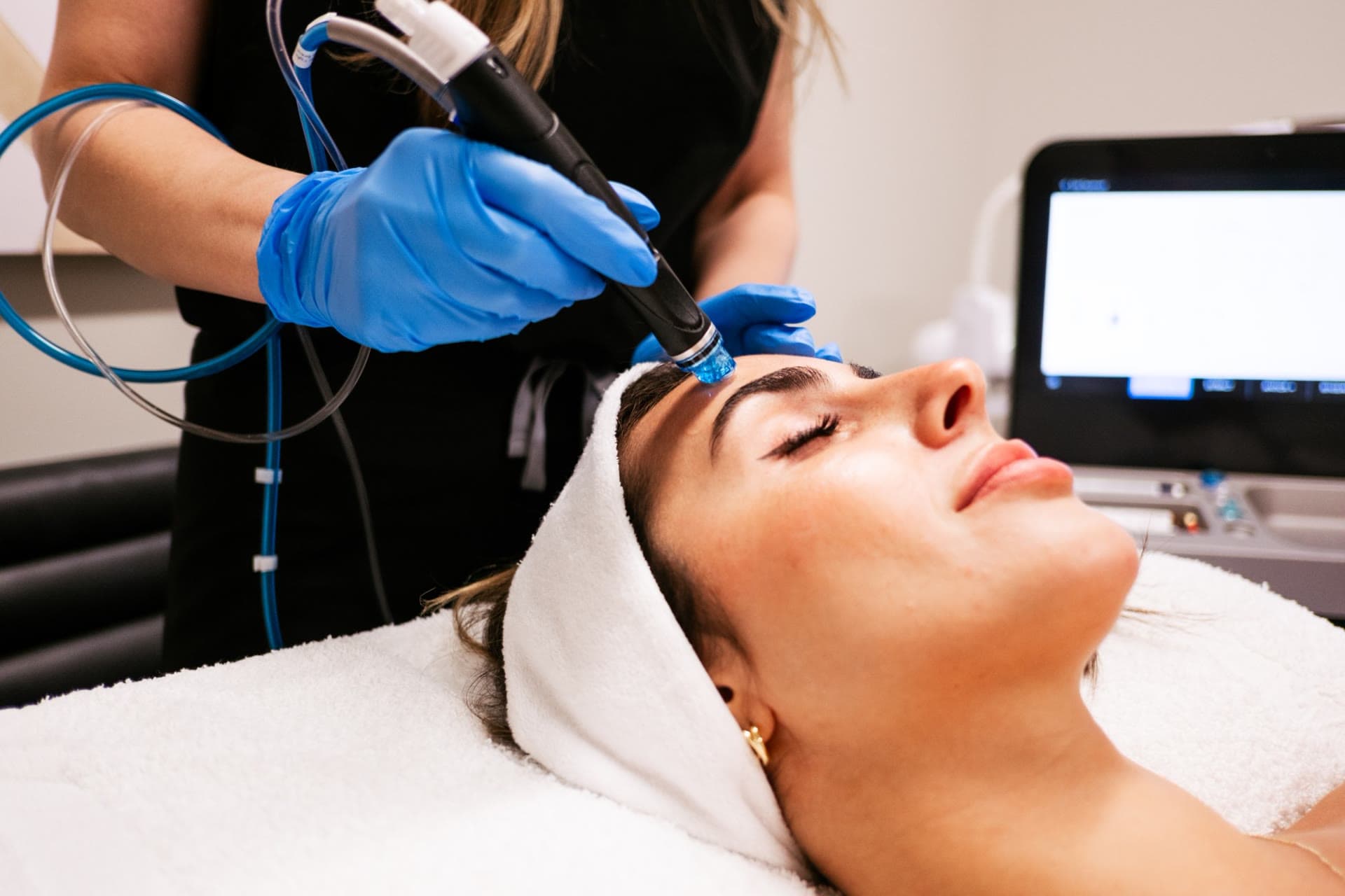 An aesthetician glides a HydraFacial tip across a relaxed patient's forehead