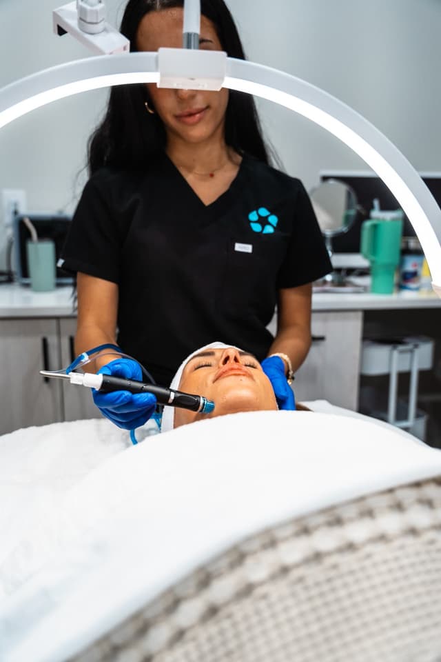 An aesthetician works under a ring light during a HydraFacial