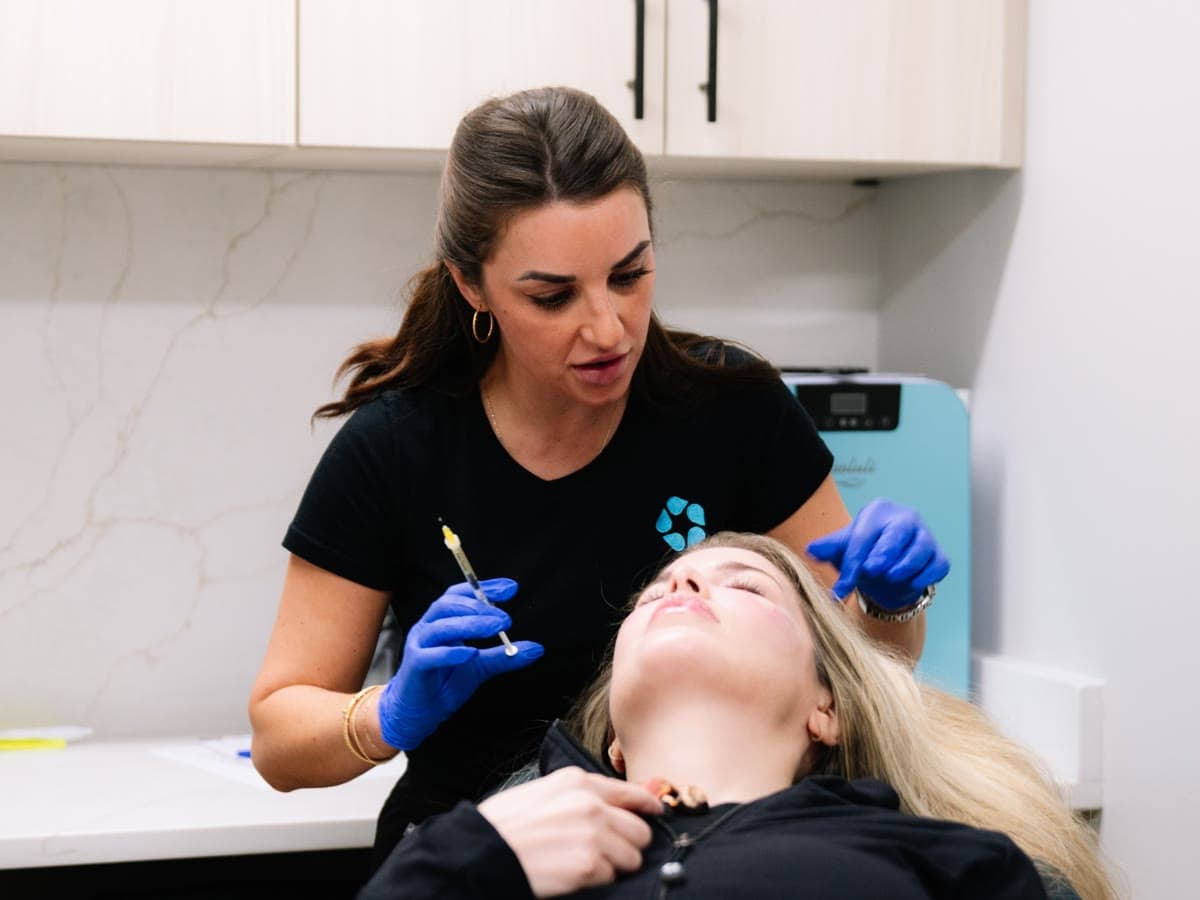 An injector explains the plan to a reclining patient before jawline treatment