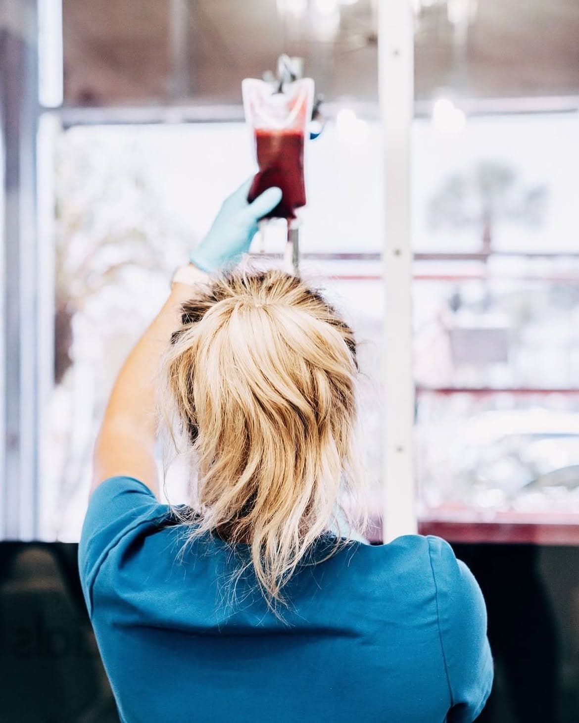 A clinician in blue nitrile gloves adjusts an ozonated blood bag on an IV pole at Relive Health Stuart