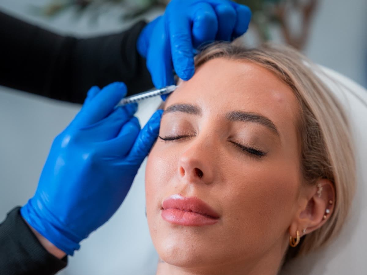 An injector places a wrinkle relaxer in a relaxed patient's forehead